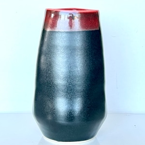 May include: A black ceramic vase with a red rim. The vase has a glossy finish and a slightly irregular shape.