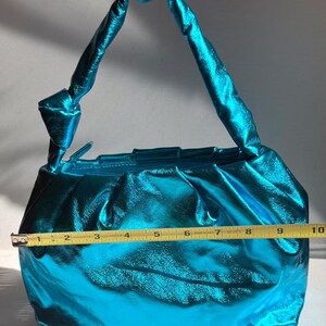 May include: A shiny, turquoise handbag with a knotted handle. The bag is approximately 10 inches wide, with a gathered design and a metallic sheen. The handle is also turquoise and knotted at the base.