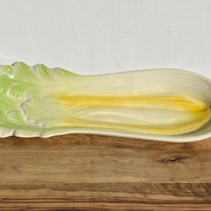 May include: A ceramic serving dish shaped like a celery stalk. The dish is white with green and yellow accents.