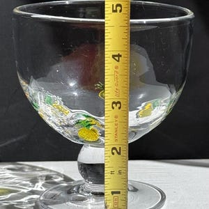 May include: A clear glass goblet with a wide bowl and a short stem. The goblet is decorated with yellow and green pineapple designs around the rim. The height of the goblet is approximately 5 inches.