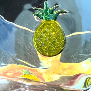 May include: A decorative pineapple with a green crown and a yellow body. The pineapple has a textured surface and is set against a colorful, abstract background with shades of blue, yellow, and orange.