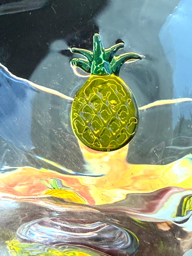 May include: A decorative pineapple with a green crown and a yellow body. The pineapple has a textured surface and is set against a colorful, abstract background with shades of blue, yellow, and orange.
