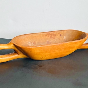 May include: A wooden serving bowl with two handles. The bowl is light brown and has a smooth, polished finish.