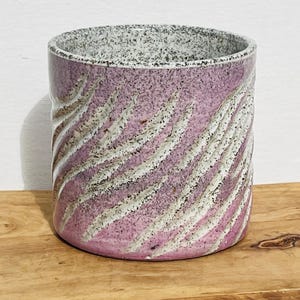 May include: A pink and white ceramic planter with a swirling pattern. The planter has a speckled glaze and a rounded shape.