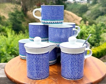 May include: A collection of ceramic mugs and lidded containers featuring a blue and white mosaic tile pattern. The pieces have a white interior and a decorative band of small dark blue shapes near the base. Some items include white lids.