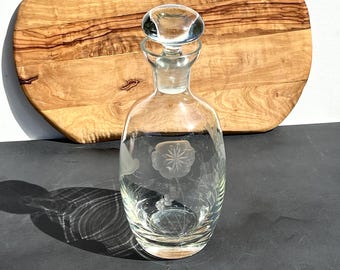 May include: A clear glass decanter with a stopper. The decanter has an etched floral design.
