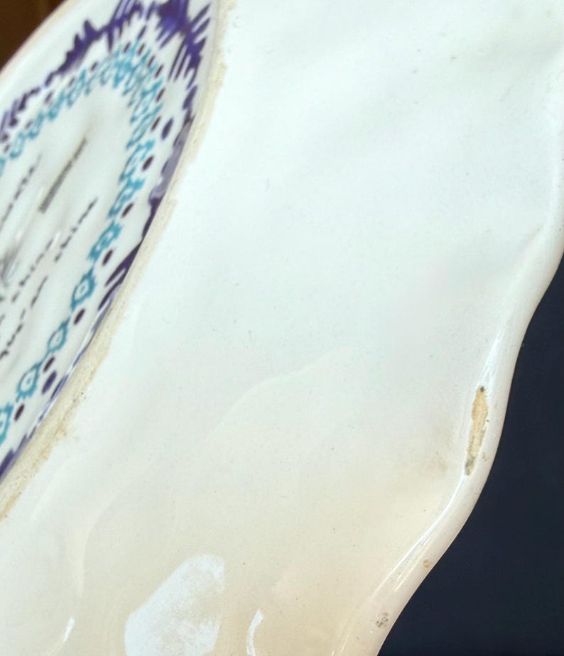 Puede incluir: Primer plano de un plato de cer&aacute;mica blanca con borde curvo. El plato presenta un patr&oacute;n geom&eacute;trico azul y morado en el borde. El plato tiene un acabado brillante y una forma ligeramente irregular.