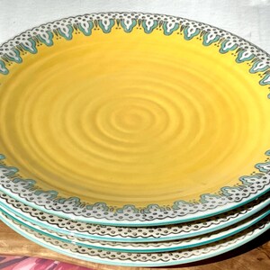 K&ouml;nnte beinhalten: Ein Set aus vier gelben Keramik-Dinnertellern mit einem blauen und wei&szlig;en Muster am Rand. Die Teller haben ein dezentes Spiraldesign in der Mitte.