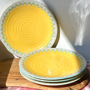 K&ouml;nnte beinhalten: Set aus vier gelben Keramik-Dinnertellern mit einem blauen und wei&szlig;en Muster am Rand. Die Teller haben eine geriffelte Textur.