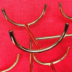 May include: Close-up of a gold-coloured metal decorative stand with curved arms and a red background. The stand has a modern design with multiple curved elements.