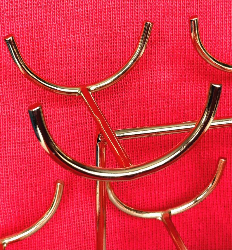 May include: Close-up of a gold-coloured metal decorative stand with curved arms and a red background. The stand has a modern design with multiple curved elements.