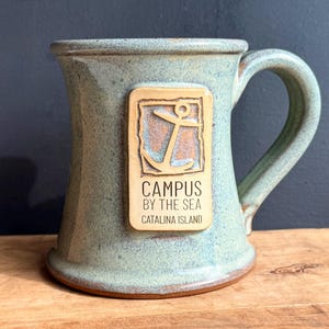 May include: A white ceramic mug with a black handle and the text "But First, Coffee" in a black, bold font. The mug is on a white surface. The mug is approximately 4 inches tall.
