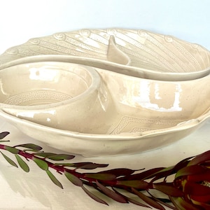 May include: A white ceramic serving dish with two sections. The dish is shaped like a yin yang symbol and has a textured design.
