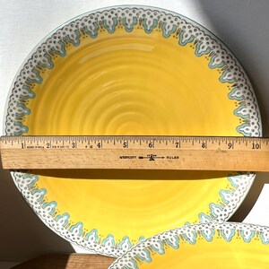 K&ouml;nnte beinhalten: Gelber Keramik-Dinnerteller mit blau-wei&szlig;em Muster am Rand. Der Teller hat einen Durchmesser von 23 cm.