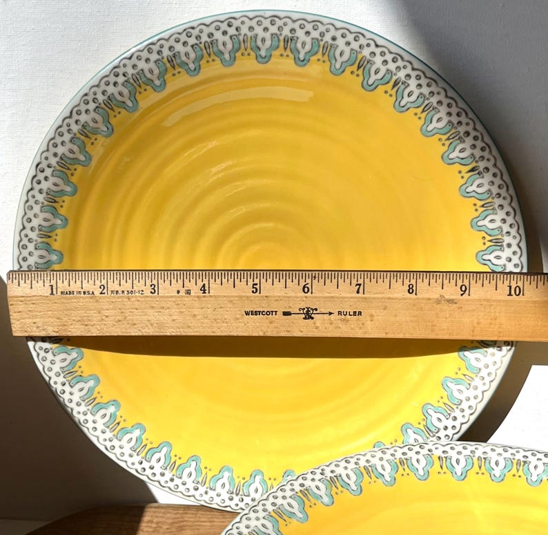 K&ouml;nnte beinhalten: Gelber Keramik-Dinnerteller mit blau-wei&szlig;em Muster am Rand. Der Teller hat einen Durchmesser von 23 cm.