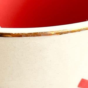 May include: A white ceramic mug with a gold rim and a red and pink design. The mug is empty and the inside is red.