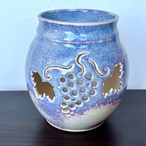 May include: A blue and white ceramic candle holder with a grapevine design. The holder has cutouts in the shape of grapes and leaves.