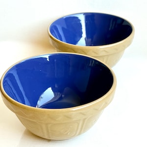 May include: Two ceramic bowls featuring a deep cobalt blue interior and a light tan exterior. The outer surface of each bowl displays a subtle embossed geometric pattern around the rim and a grid-like texture on the lower body of the vessel.