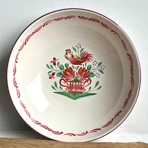 May include: A white ceramic bowl with a red rim and a hand-painted design of a rooster in a flower pot. The bowl has a red and white border.