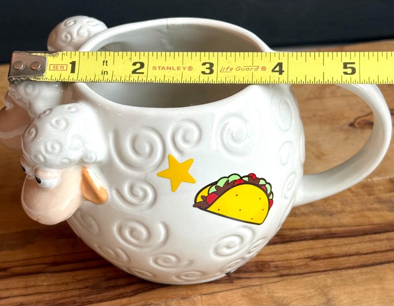 May include: White ceramic sheep-shaped mug with a handle. The mug features a yellow star and a taco graphic. The mug is approximately 4 inches in diameter.