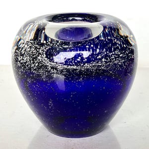 May include: A cobalt blue glass vase with a white speckled design. The vase has a round shape and a wide opening.