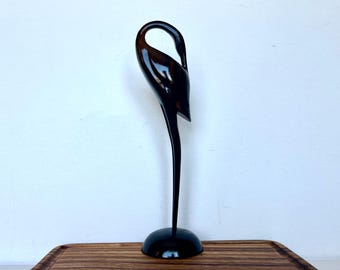 May include: A black wooden sculpture of a bird with its head bent down. The sculpture is standing on a wooden base.