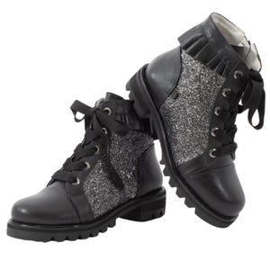 Può includere: Stivali in pelle nera con dettagli in glitter argento e chiusura con lacci. Gli stivali hanno una suola robusta e un dettaglio arricciato sulla parte superiore.