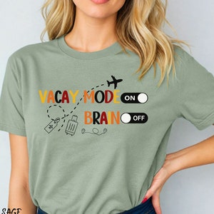 Funny travel shirt with toggle on switch next to "vacay mode" and toggle off switch next to "brain". Adorned with graphics of an airplane, luggage, and luggage tag. Bella and Canvas 3001 crew neck t-shirt.