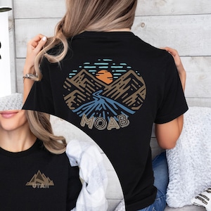 May include: Black t-shirt featuring a circular graphic on the back with a mountain and river scene, the word "MOAB" below. The front of the shirt has a smaller mountain graphic with the word "UTAH".