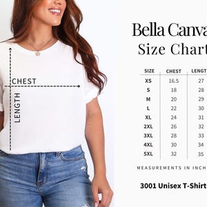 Puede incluir: Una camiseta unisex blanca Bella Canvas con una tabla de tallas. La tabla enumera las medidas de pecho y largo en pulgadas para las tallas XS a 5XL. La modelo lleva la camiseta y unos vaqueros azules.