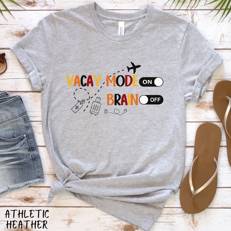 May include: Grey t-shirt with the text "Vacay Mode On" and "Brain Off" with a toggle switch graphic next to each phrase. The graphic also includes a suitcase, a plane, and a tag.