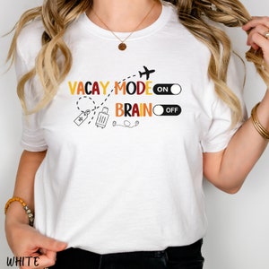 May include: White t-shirt with a graphic design that says "Vacay Mode On" and "Brain Off" with a suitcase, aeroplane, and toggle switches.