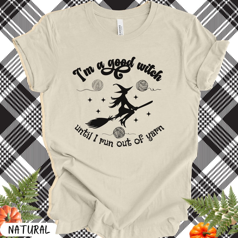 May include: A cream-colored t-shirt with the text "I'm a good witch until I run out of yarn" in black script. A witch on a broom is in the center, with yarn balls and stars. The shirt is a natural color.
