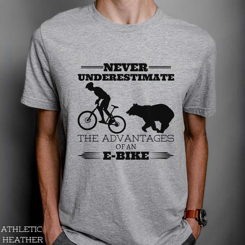 Crew neck t-shirt adorned with a man riding an E-Bike and a bear chasing behind, and the phrase, "Never underestimate the advantages of an E-Bike"