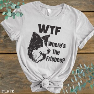 May include: A light gray t-shirt with a black and white illustration of a border collie dog. The text "WTF Where's The Frisbee?" is printed on the shirt.