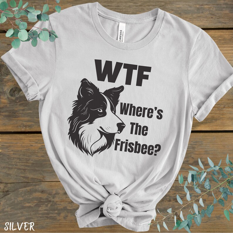 May include: A light gray t-shirt with a black and white illustration of a border collie dog. The text "WTF Where's The Frisbee?" is printed on the shirt.