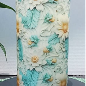 May include: A white pillar candle with a floral design. The candle features a raised, embossed design of white flowers with teal leaves.
