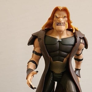 May include: A brown and black action figure of a character with long blonde hair and a brown coat. The figure has a menacing expression and is holding a red and white object in its hand.