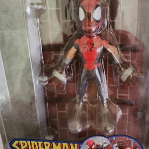 Peut inclure: Une figurine d'action rouge et noire de Spider-Man dans un style manga. La figurine est pos&eacute;e les bras tendus et se tient debout sur un mur de briques. L'emballage comprend le texte "Spider-Man Manga Spider-Man".