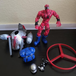 May include: A red and black Spider-Man action figure with blue boots, surrounded by various accessories. Accessories include a silver and red spider-themed device, a blue chest piece, a red propeller, a silver helmet, and a black and silver weapon.