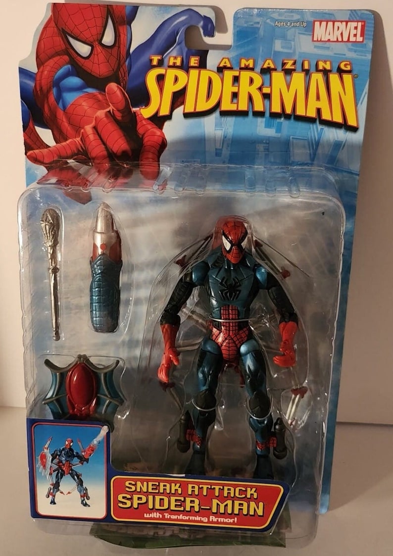 May include: A plastic package containing a red and blue action figure of Spider-Man with transforming armour. The figure is holding a web shooter in each hand. The package also includes a red and blue web shooter and a silver staff. The package is labelled "The Amazing Spider-Man" and "Sneak Attack Spider-Man with Transforming Armour!"
