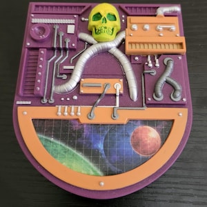 May include: A purple and orange decorative panel featuring a yellow skull, silver tubing, and a space scene. The panel has a retro, sci-fi aesthetic with detailed mechanical elements and a planetary backdrop.
