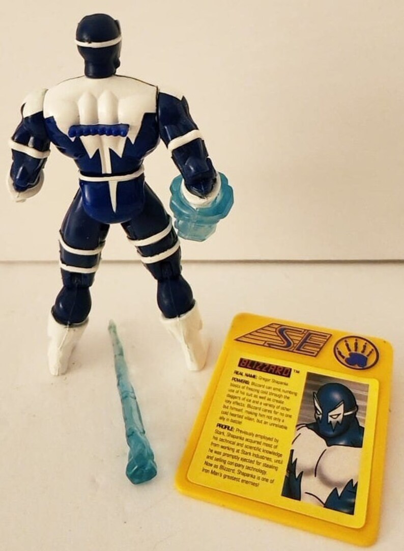 Op de afbeelding: Een blauwe en witte action figure van Blizzard, een superheld uit het Marvel-universum. De figuur houdt een blauw ijswapen vast. De figuur staat op een wit oppervlak. De kaart op de achtergrond heeft de naam van het personage en zijn krachten.