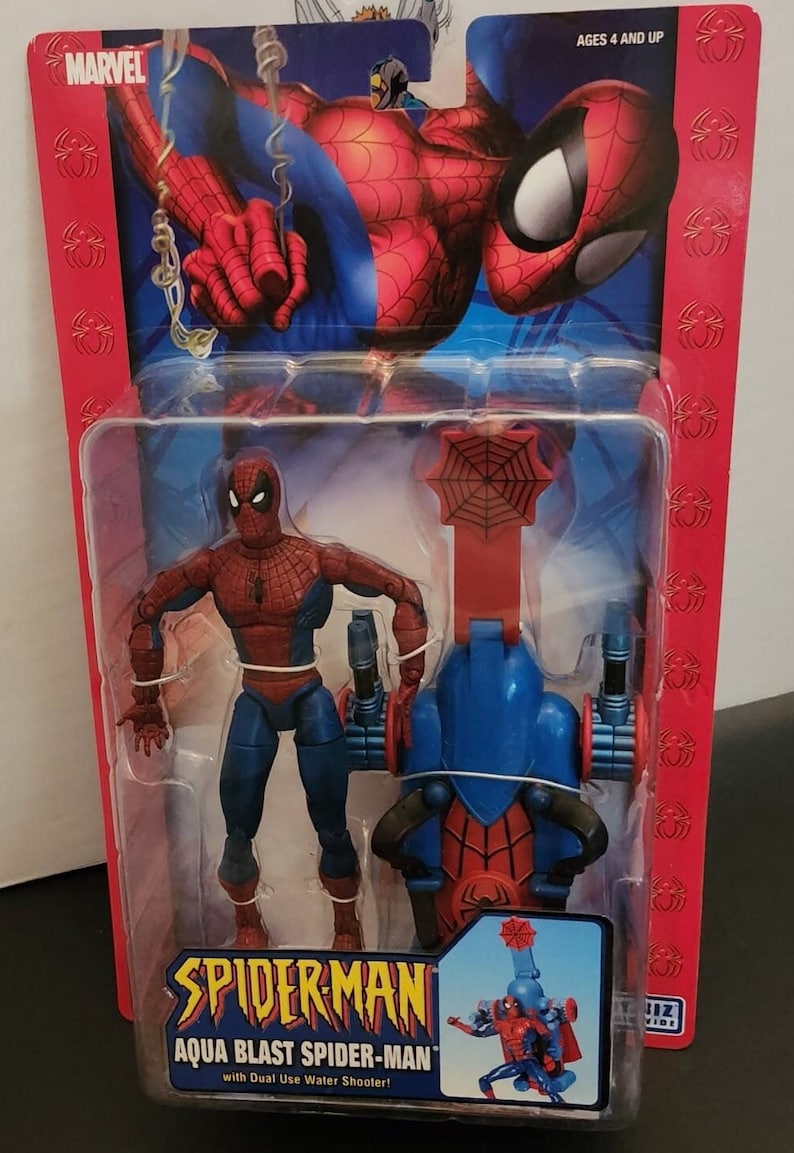 May include: A red and blue action figure of Spiderman with a water shooter. The figure is packaged in a red and blue box with the words "Spiderman Aqua Blast Spider-Man with Dual Use Water Shooter!" on the front.