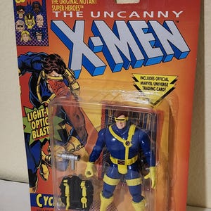 Op de afbeelding: Een Cyclops actiefiguur van de X-Men, verpakt op een rood en gele kaart. De figuur draagt een blauw en geel uniform met een geel vizier. De verpakking bevat het Marvel Comics-logo en de tekst "The Uncanny X-Men".