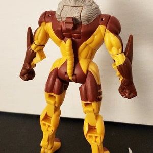 May include: A yellow and brown action figure of a character with a gray fur collar. The figure has a long tail and is posed with its arms at its sides.