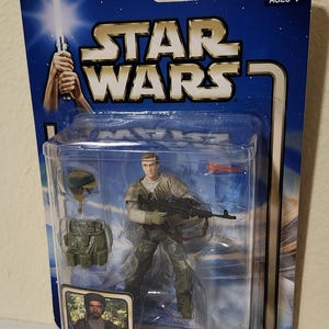 Puede incluir: Figura de acción de Star Wars de un soldado rebelde de Endor, empaquetada en una funda de plástico transparente. La figura viste un uniforme verde y beige y sostiene un rifle. El embalaje incluye el texto "Return of the Jedi" y una advertencia sobre piezas pequeñas.