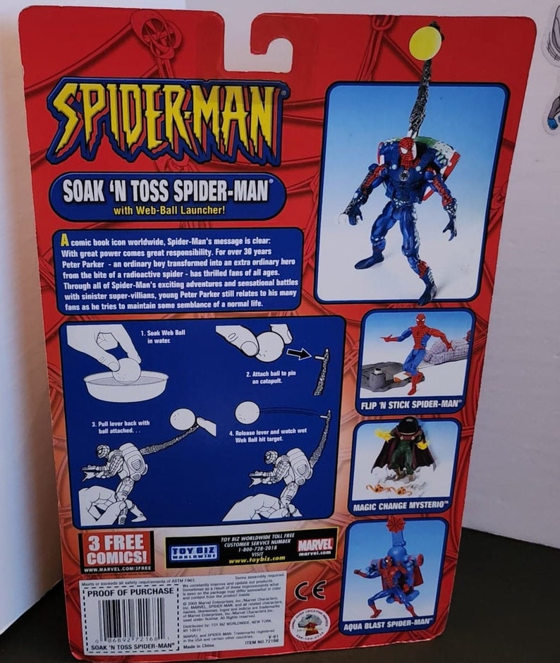 May include: A red, blue, and black Spider-Man action figure with a web-ball launcher. The figure is packaged in a cardboard box with a red background and the words "Soak 'N Toss Spider-Man" printed on it. The box also features images of other Spider-Man figures, including Flip 'N Stick Spider-Man, Magic Change Mysterio, and Aqua Blast Spider-Man.