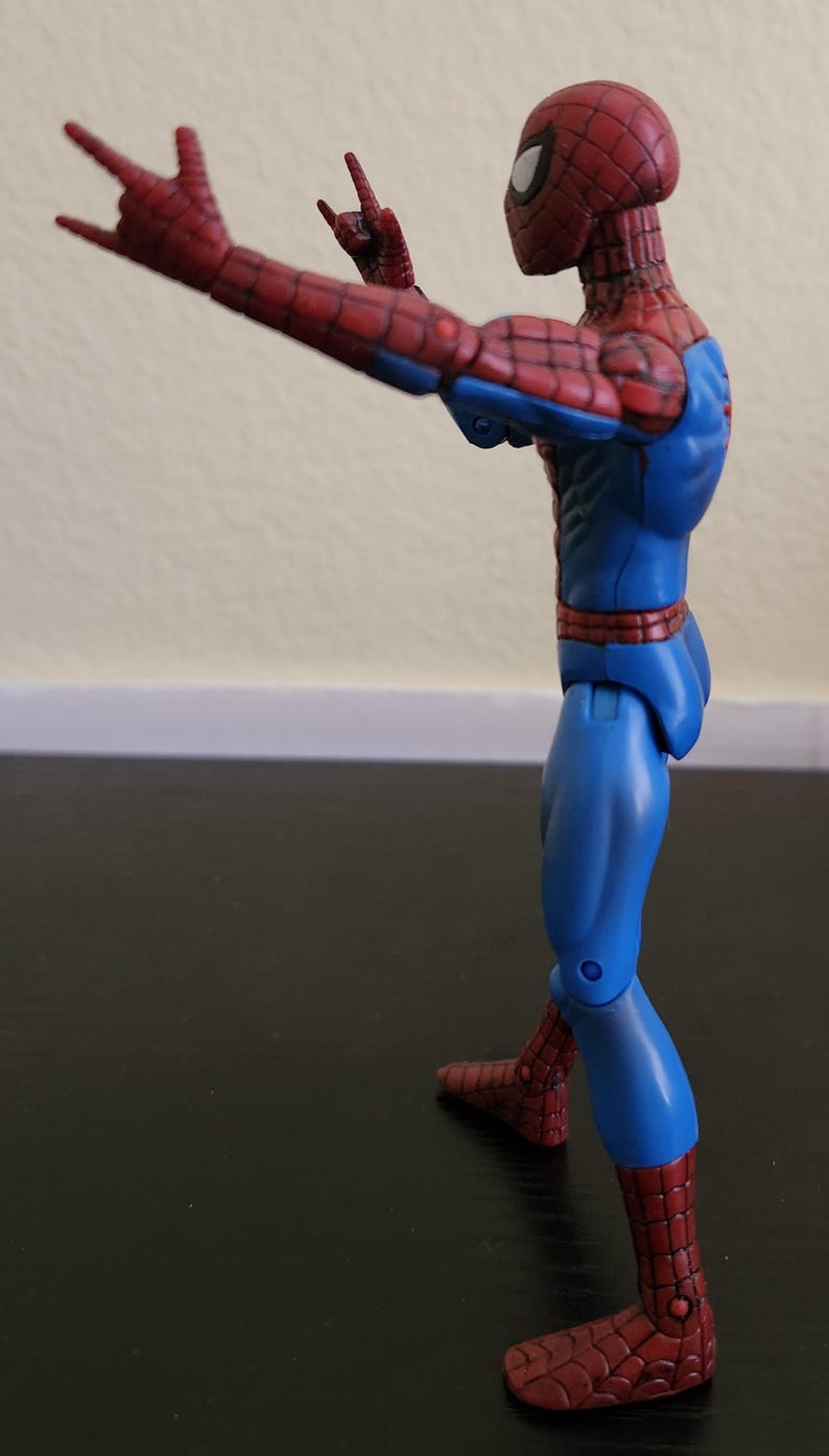 May include: A Spider-Man action figure in a dynamic pose, viewed from the side. The figure is predominantly blue and red, with a detailed web pattern on the red sections. The figure is striking a hand gesture.