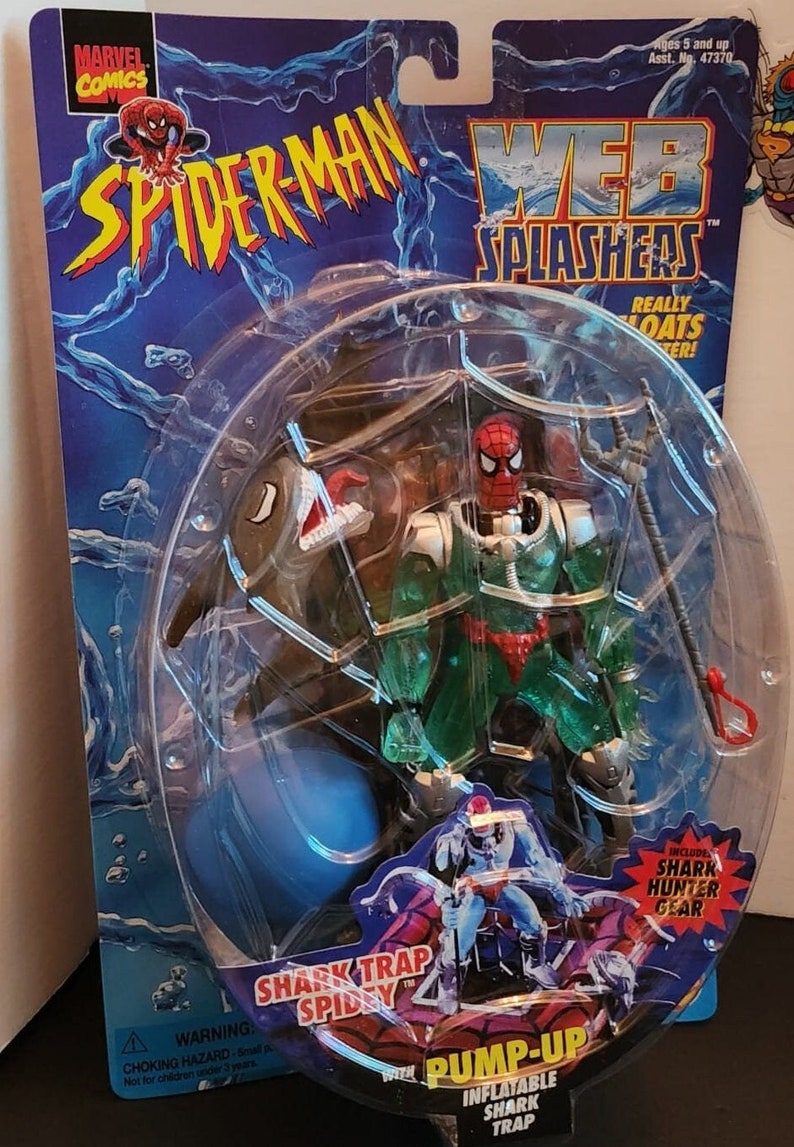 May include: Spider-Man action figure in packaging. The figure is in a clear plastic bubble, with a blue and red Spider-Man design. The packaging includes the text "Spider-Man", "Web Splashers", and "Shark Trap Spidey". Includes Shark Hunter Gear.